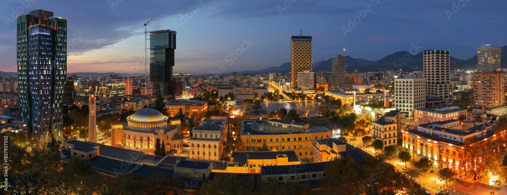 Obraz premium Aerial twilight panorama of central Tirana showcasing its illuminated skyline, modern towers, and historic landmarks