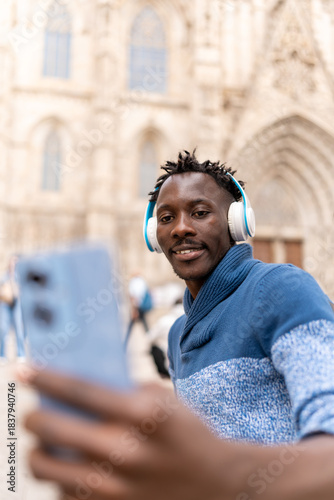 African American man smiling, taking self portrait with smartphone while listening music outdoors