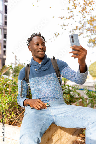 African American man smiling, taking selfie with mobile phone in city park