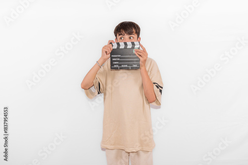 young casual dressed Generation Z influencer white male model teenage boy prepares to create and direct social media film reel with blank clapperboard slate. plain background studio setting