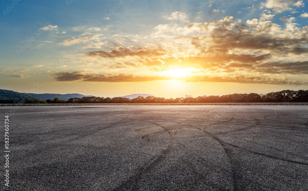 Naklejka premium Asphalt race track road and tire track with dramatic sky clouds at sunset
