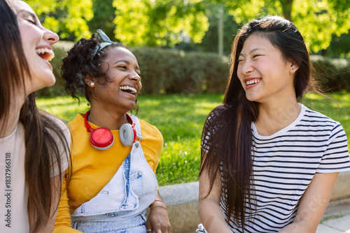 Three young diverse women laughing together outside, having fun enjoying day off at city park. Female friendship concept