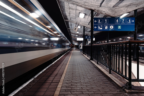 Train speeding through urban station platform at night
