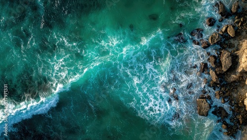 An aerial view showcases crashing teal waves along a rocky shoreline, creating a textured contrast