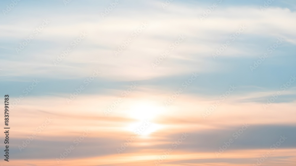Fototapeta premium Soft pastel sunlight spreads through delicate layered clouds, creating a calm, dreamy sky in warm peach and cool blue tones at the horizon.