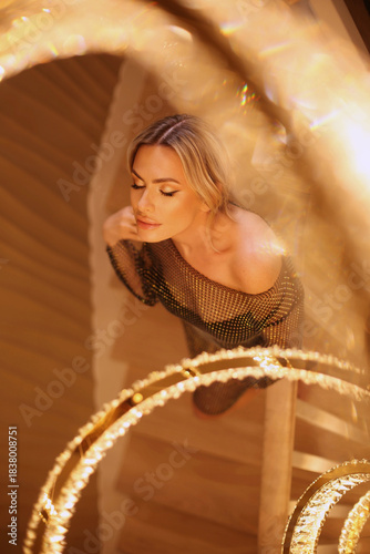Sexy blond model alluring in bright dress in royal luxury interior with golden chandelier