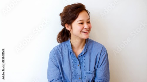 Young woman smile portrait blue shirt casual natural light relaxed seated against white wall cheerful happy expression