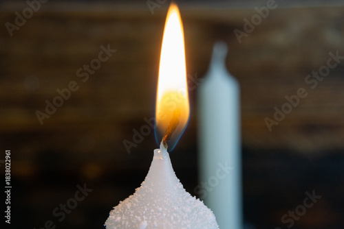 A close-up macro shot of a white candle burning softly, with detailed wax texture and a glowing flame.