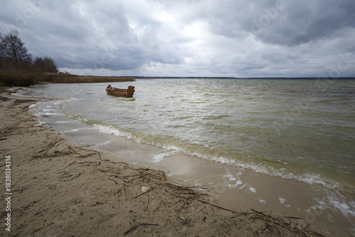 Old rural wooden, fishing boat is moored on the shore of a lake. A gloomy windy day