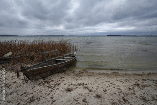 Old rural wooden, fishing boat is moored on the shore of a lake. A gloomy windy day