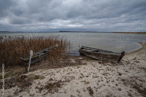 Old rural wooden, fishing boat is moored on the shore of a lake. A gloomy windy day