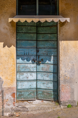 Rustic charm and history captured in this old wooden door painted in blue and green, with paint chipped away by time and an authentic rusty padlock.