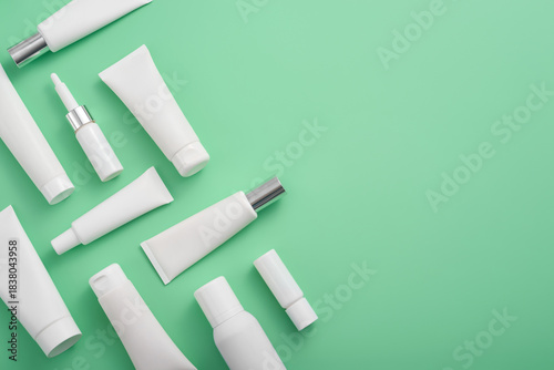 Assortment of white cosmetic containers and tubes displayed on a light green background creates beauty and self care vibe