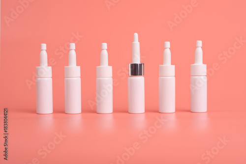 Seven white nasal spray bottles arranged on a flat pink surface, one with a silver accent