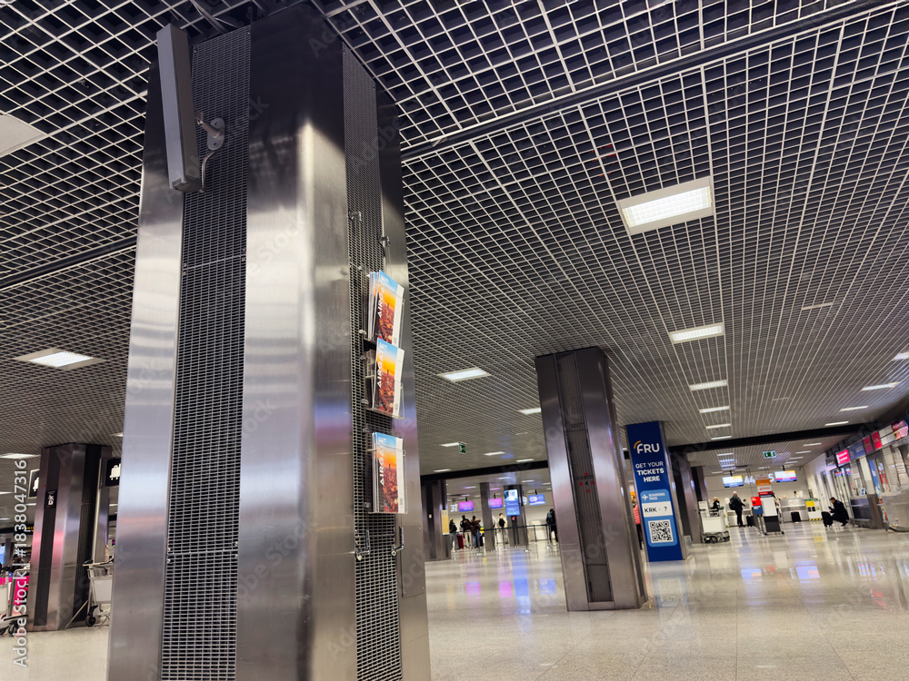 Naklejka premium Modern Krakow airport terminal in Poland with metallic columns posters and travelers in the distance