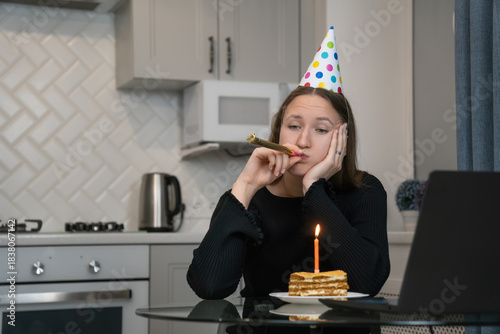Fotografie Young woman wearing party hat blowing in blowing a festive horn and looking bore