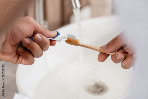 Hands putting toothpaste on a bamboo toothbrush for daily dental hygiene