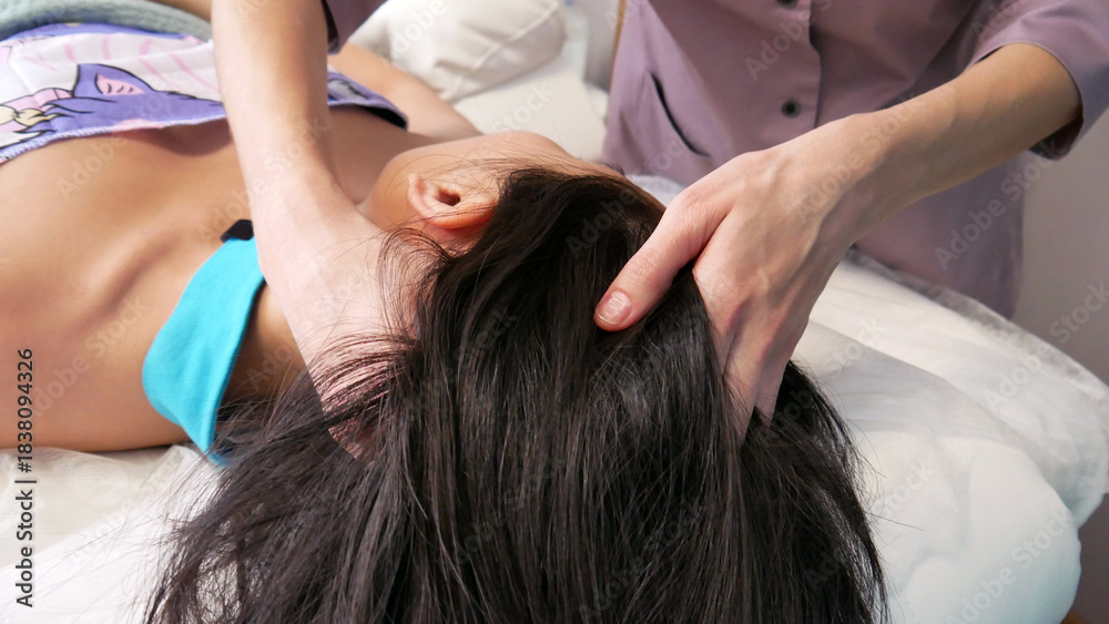 Fototapeta premium Close-up of a masseuse's hands giving a head massage to a long-haired girl
