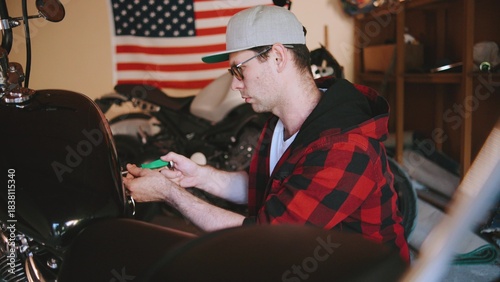 Fényképezés Mechanic working on a motorcycle in a garage while an American flag hangs in the
