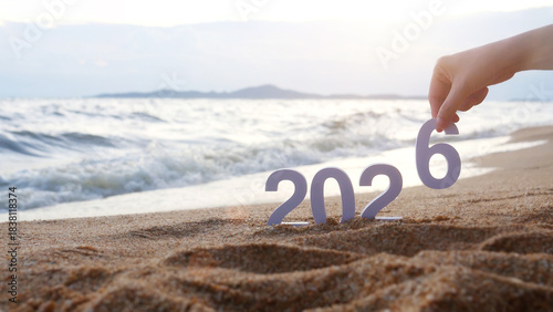 hand place the number 6 on sandy beach, transition from year 2025 to 2026 for new year sign on summer beach at sunset time, with ripple sea wave and beautiful nature at background, New Year celebrate