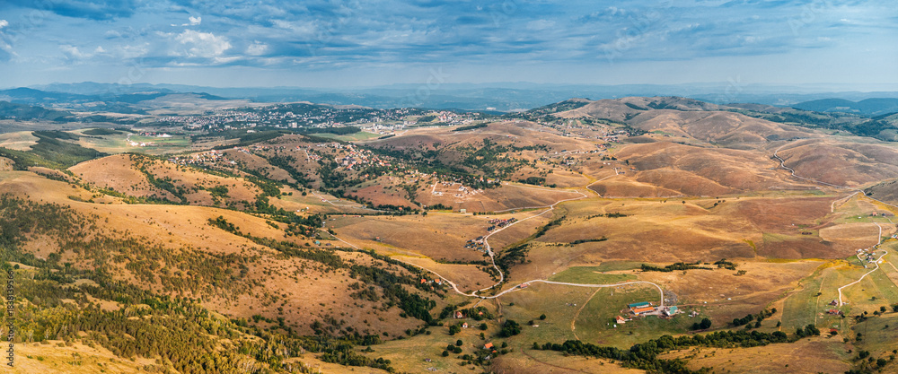 Naklejka premium Expansive aerial view showcasing dry rolling hills, green valleys, scattered villages, and a distant town under a cloudy sky