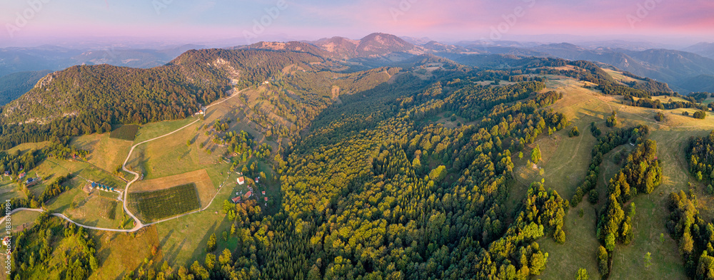 Naklejka premium Aerial panorama showing winding roads, houses, and cultivated fields nestled in a mountain valley during golden hour
