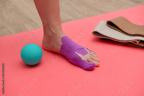 Woman with kinesiology tape on her foot with myofascial release ball on a pink gym mat. Treatment for hallux valgus, sport.
