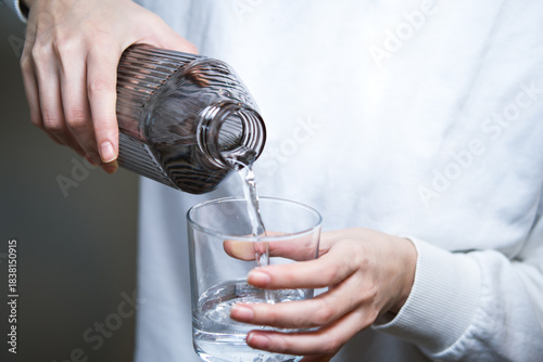 Woman's hand pouring water from a jug into a transparent glass.