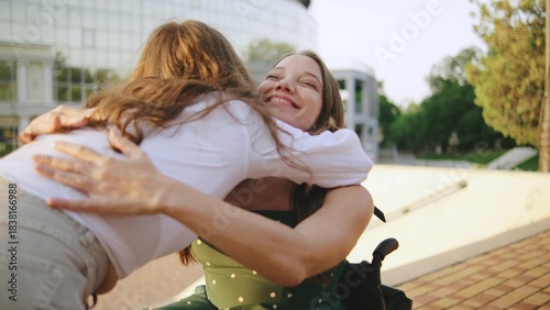 two female multiracial friends one inclusive woman in a wheelchair share a warm embrace outdoors as a disabled woman in a wheelchair enjoys a joyful moment in the sun
