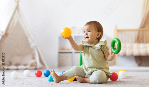Foto Smiling baby sitting on floor holding colorful ball and ring toy