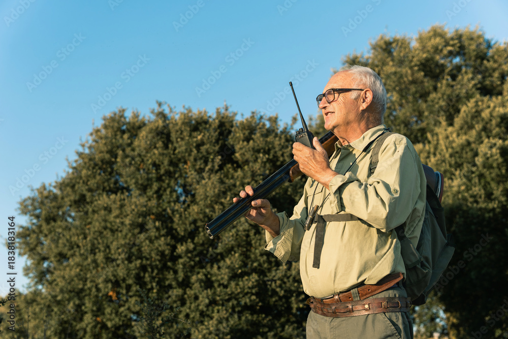 Fototapeta premium Senior hunter carrying shotgun and walkie talkie looking for prey