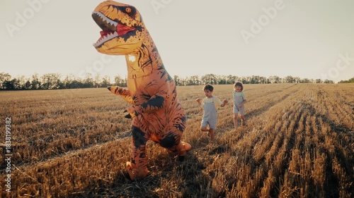 Inflatable Dinosaur T-Rex is Chased, running from Little Kids Boys in field.