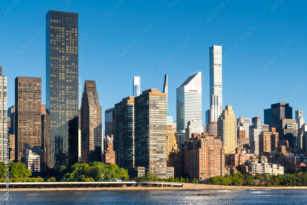 Fototapeta premium Midtown East Manhattan skyline seen across the East River, with modern skyscrapers and high-rise buildings in morning light. New York City, USA