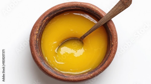 Ghee or clarified butter in a traditional clay bowl with a spoon, isolated on white