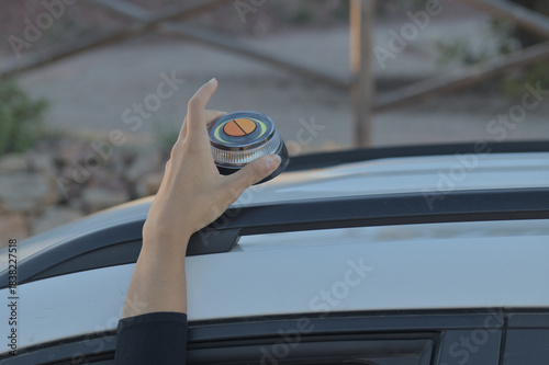 Hand placing a V16 emergency beacon on the roof of a broken-down vehicle. The emergency flasher is mandatory for replacing triangles in Europe. DGT Spain.