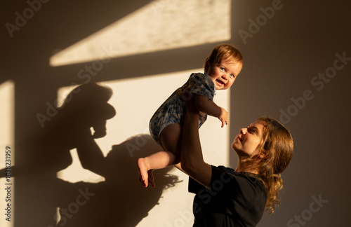 Silhouette and shadows on the wall of a happy young mother and her child under one year old. The mother and baby are smiling, a Happy Mother's Day concept. Joyful motherhood. Fun games together