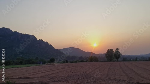 An epic view of a beautiful sunrise over the hills, in front of farmland in rural village