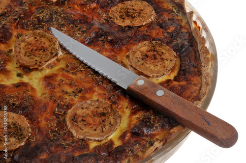 Tarte salée au fromage de chèvre dans un plat avec un couteau en gros plan sur fond blanc