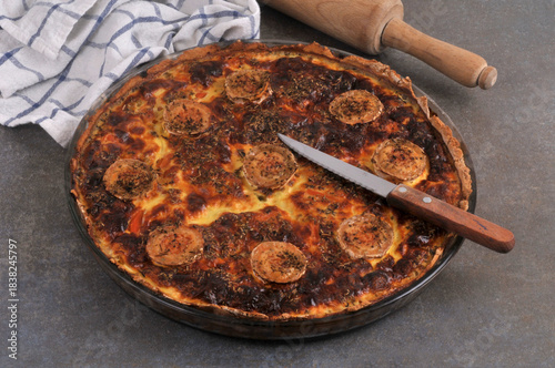 Tarte salée au fromage de chèvre dans un plat avec un couteau en gros plan sur fond gris avec un rouleau à pâtisserie et un torchon