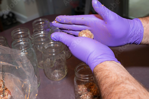 Man's gloved hands preparing glass pint jars for canning raw, pork sausage meat