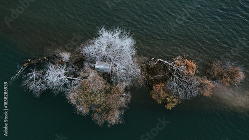 Frozen Island - Aerial View A striking aerial view of a small, isolated islet or sandbar in dark water. The trees in the center are covered in heavy white hoarfrost or snow.