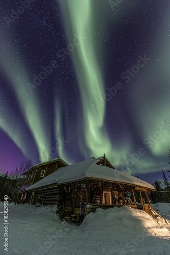 Green and purple northern lights (aurora borealis) over a log cabin in the snow, Brooks Range, Alaska, USA