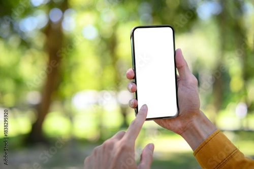 Fototapeta Naklejka Na Ścianę i Meble -  Man hand holding smartphone mockup with white screen, summer park background