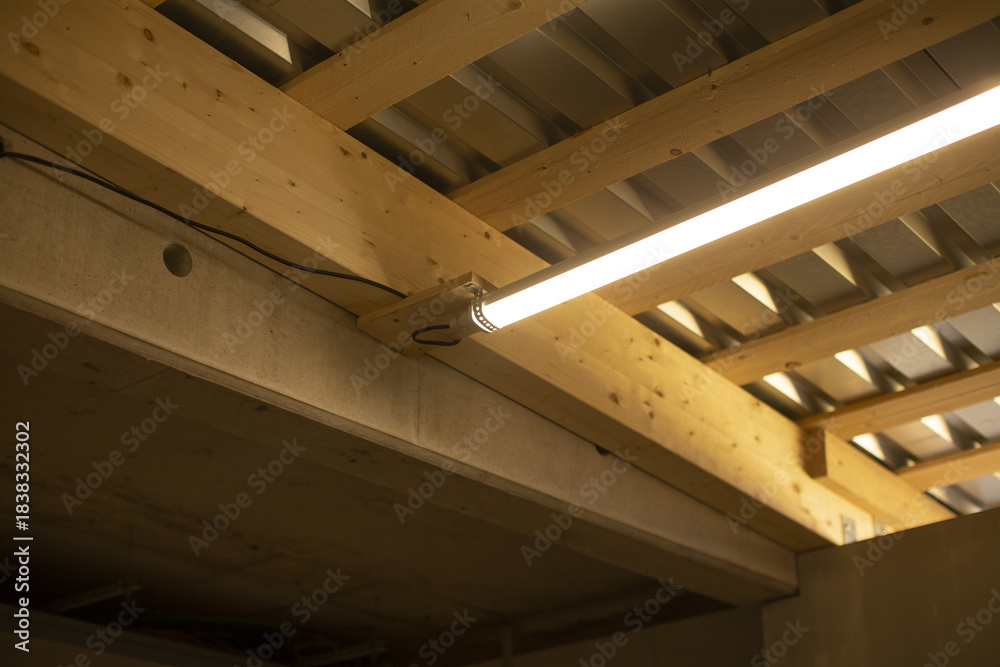 Obraz premium worksite fluorescent light under wooden beams and metal decking, bright linear illumination over timber joists and temporary