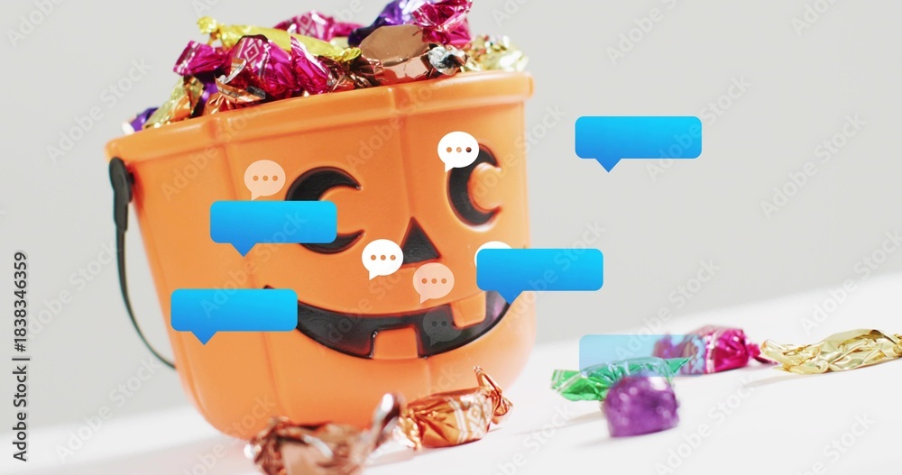 Fototapeta premium Sitting jack-o'-lantern bucket holding foil candies and wrappers on white table with chat bubbles