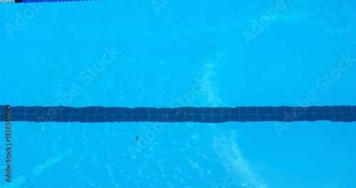 Displaying dark tiled lane marker stretching across clear blue pool interior, with scattered debris