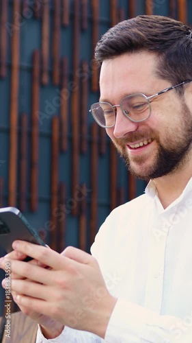 Portrait of businessman stand in city center street uses phone, texting, scrolling, typing message at sunny day. Outdoors.