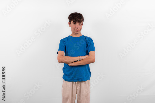 young casual dressed white male Gen Z model teenage boy, arms folded and slight smile expressing positive happy but in a nonchalant relaxed way. Blue T-shirt in plain background studio setting	