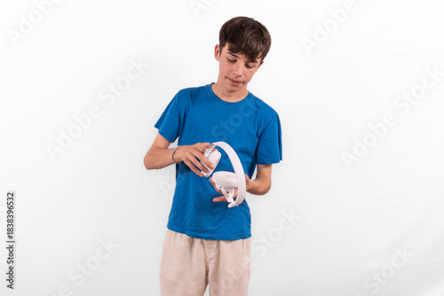 young casual dressed fun happy Gen Z influencer white male model teenage boy with wireless headphones for listening to music podcast or social media from digital device plain background studio setting