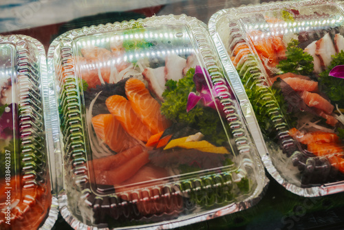 Freshly sliced salmon and tuna with herbs in a plastic container. Portion of fish packed for delivery.